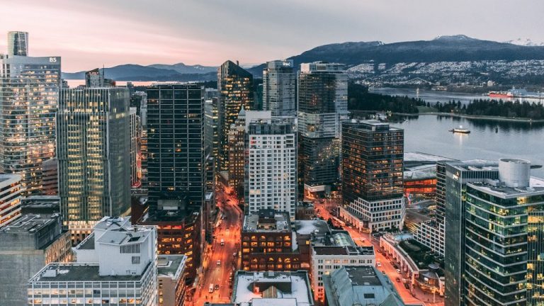 The downtown buildings of Vancouver, British Columbia at dusk with a body of water and mountains in the background