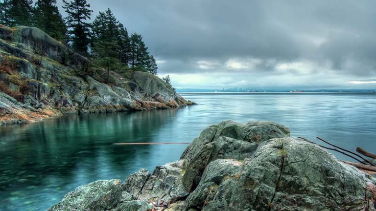 A cloudy sky over the ocean and rocky coast and evergreens of Bowen Island, British Columbia