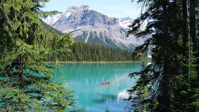 People are paddling a canoe in a lake, with trees and a mountain in the background.