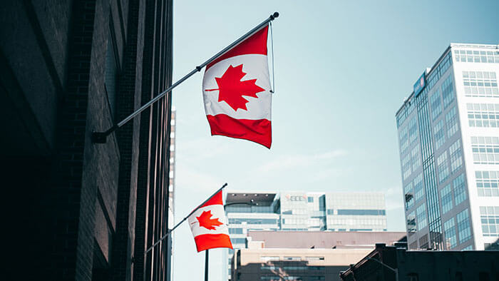 Two Canadian flags hanging from a building in a city setting.