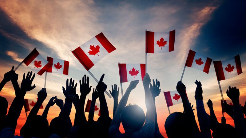 Le Canada en fête : personnes agitant des drapeaux canadiens au coucher du soleil.